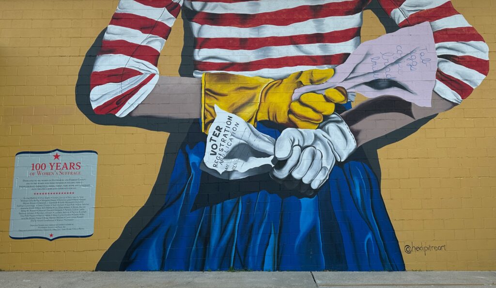 A mural in Hattiesburg, Mississippi with a painting of a woman holding a cleaning list and voter registration behind her back 