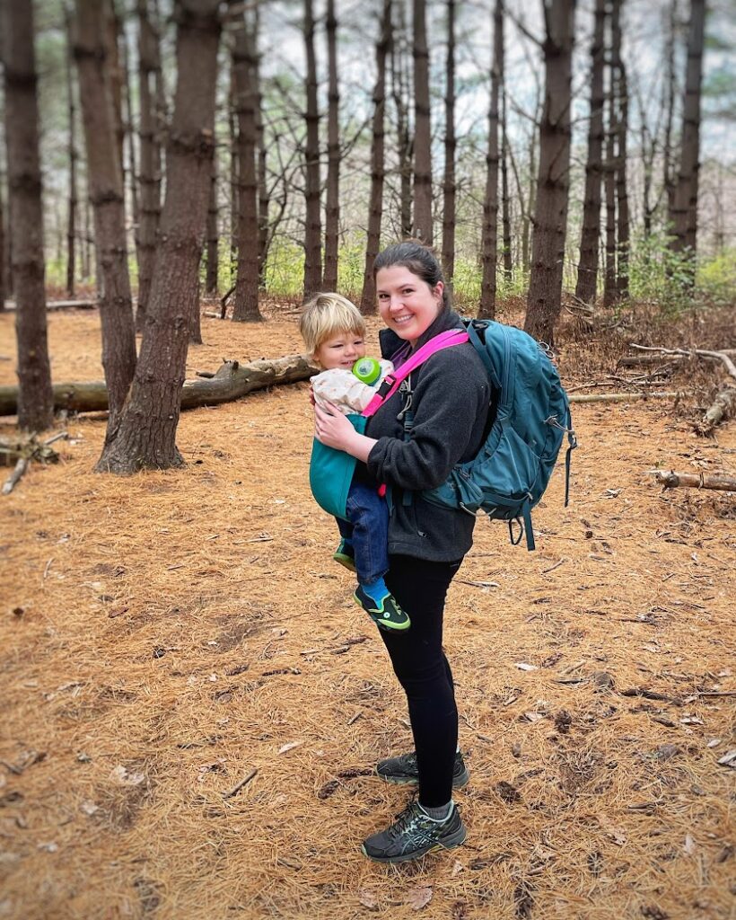 a mom in the woods wearing a trail magik carrier and a backpack, showing potential gifts for outdoorsy moms