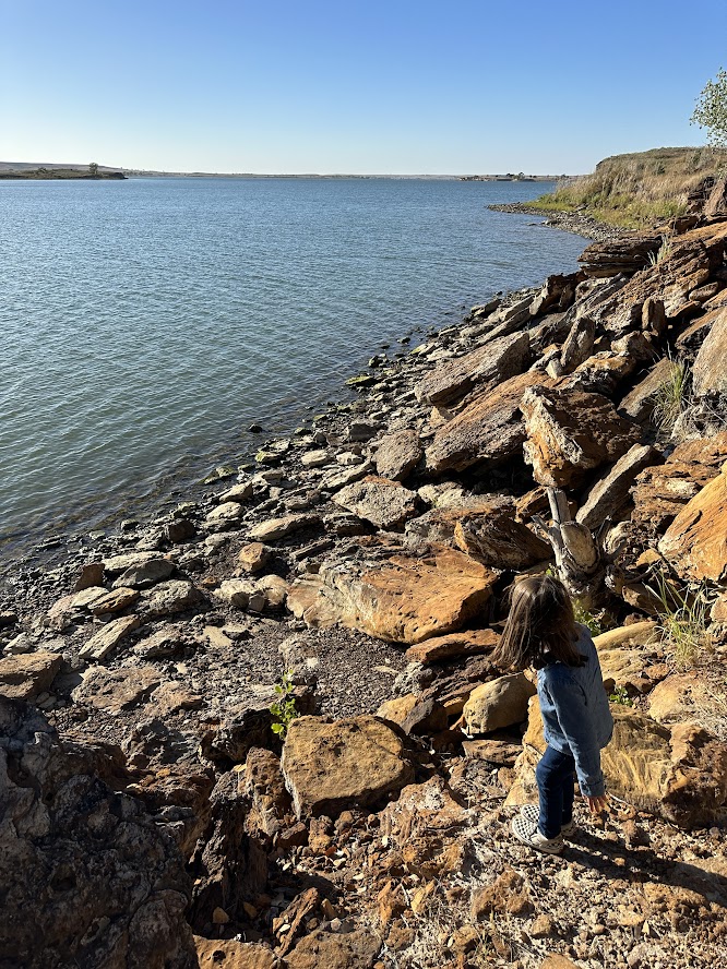 A girl walking down rocks to a beautiful blue lake