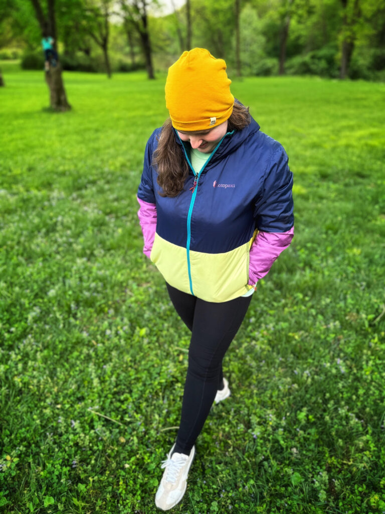 A woman walking outside looking down wearing a Cotopaxi hooded jacket