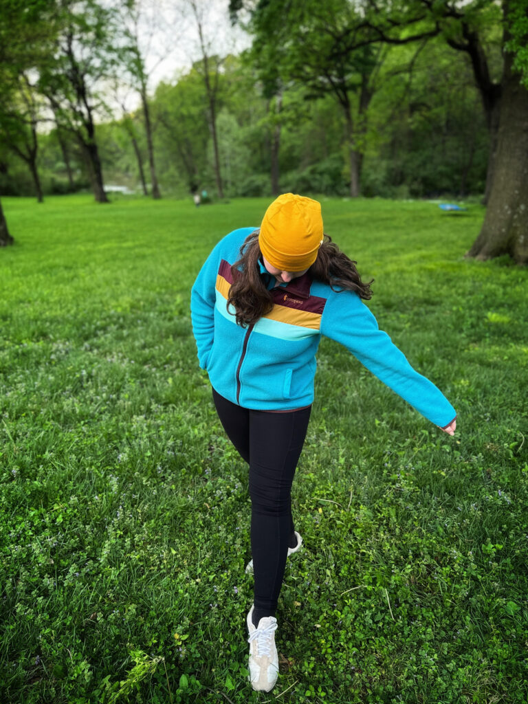 a woman walking outside looking down with one arm out wearing a Cotopaxi fleece jacket