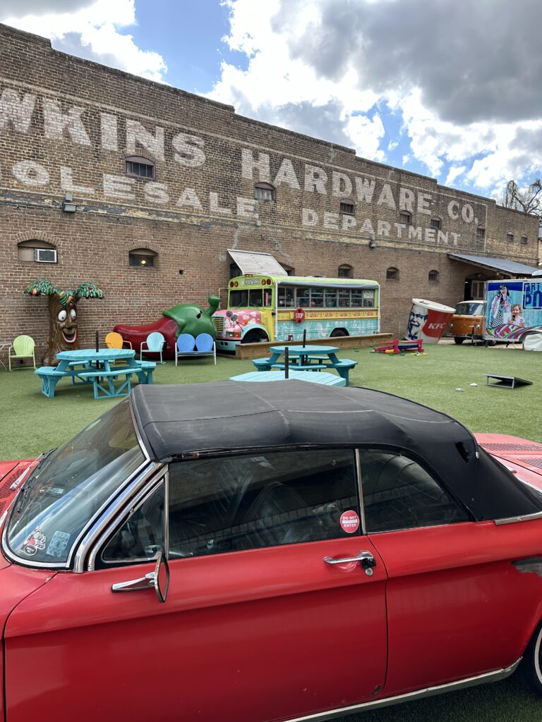 The outdoor area at the Lucky Rabbit in Hattiesburg, Mississippi with an old convertible car, an old bus, and funky pop culture items. 