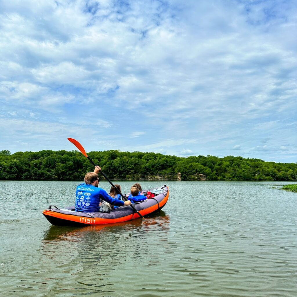 A man paddling in an inflatable canoe with kids on Lake Olathe