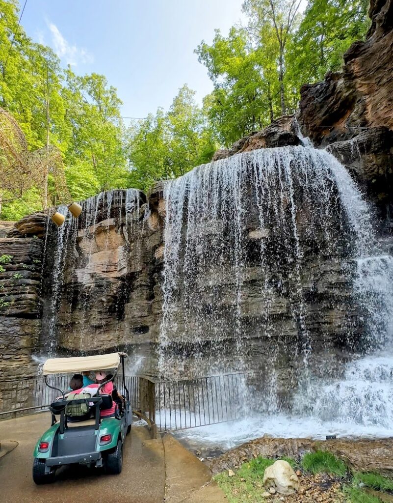 A golf cart driving by a waterfall at Lost Cave Canyon and Nature Trail