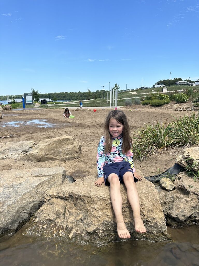 A girl smiling in front of the sand pit at Lake Olathe