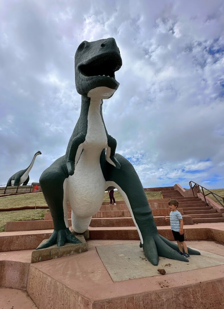 a boy standing by a dinosaur 