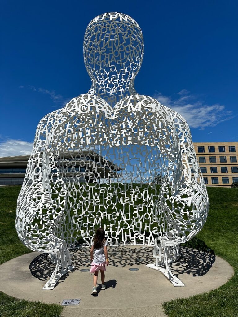 A large open sculpture made out of white letters with a girl walking into it at Pappajohn's Sculpture Park in Des Moines, Weekend Trips From Kansas City