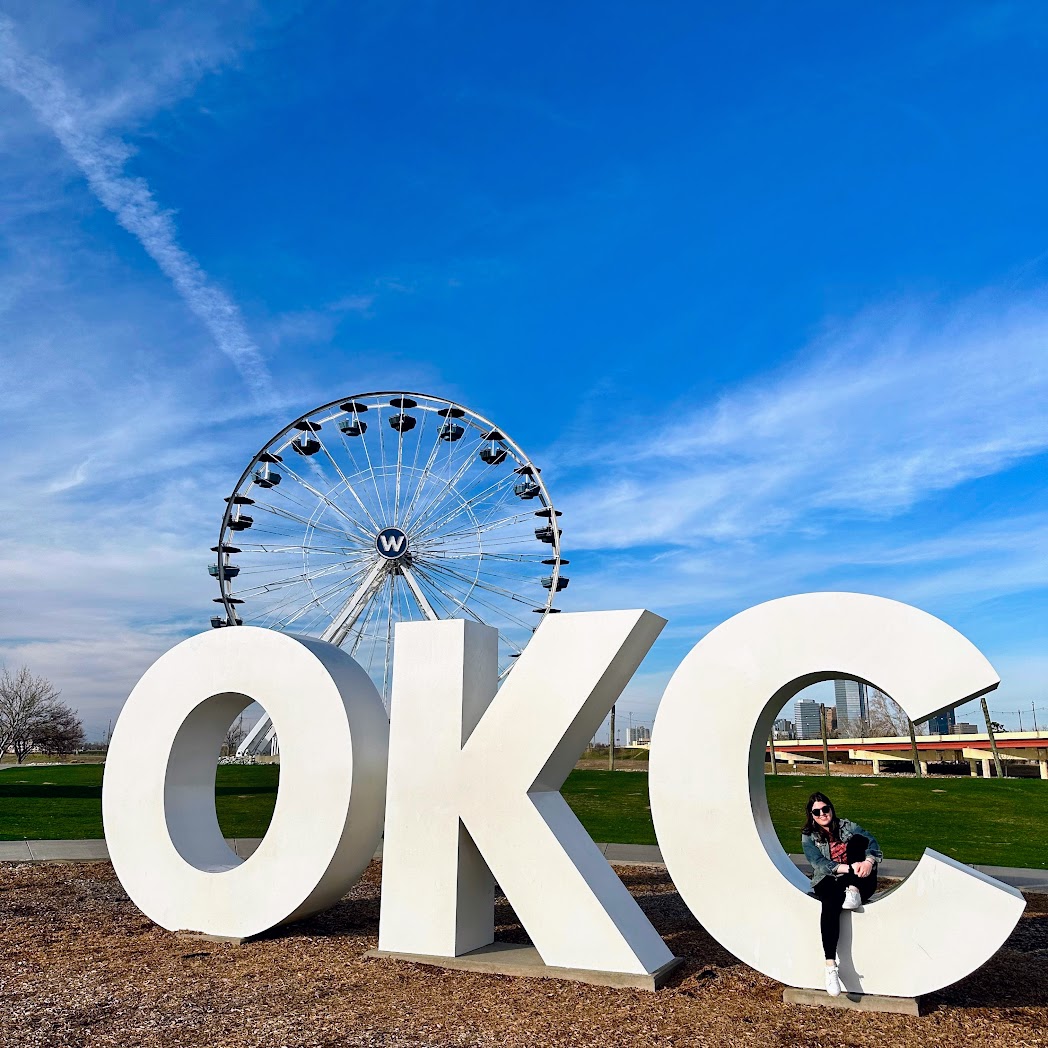 Large letters spelling "OKC" in front of a Ferris wheel at Wheeler Park in Oklahoma City, a great road trip from Kansas City