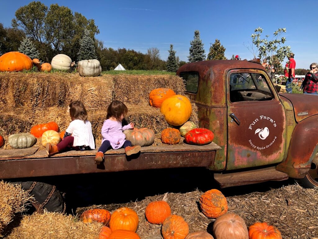 two girls sitting on the back of an old truck with pumpkins 