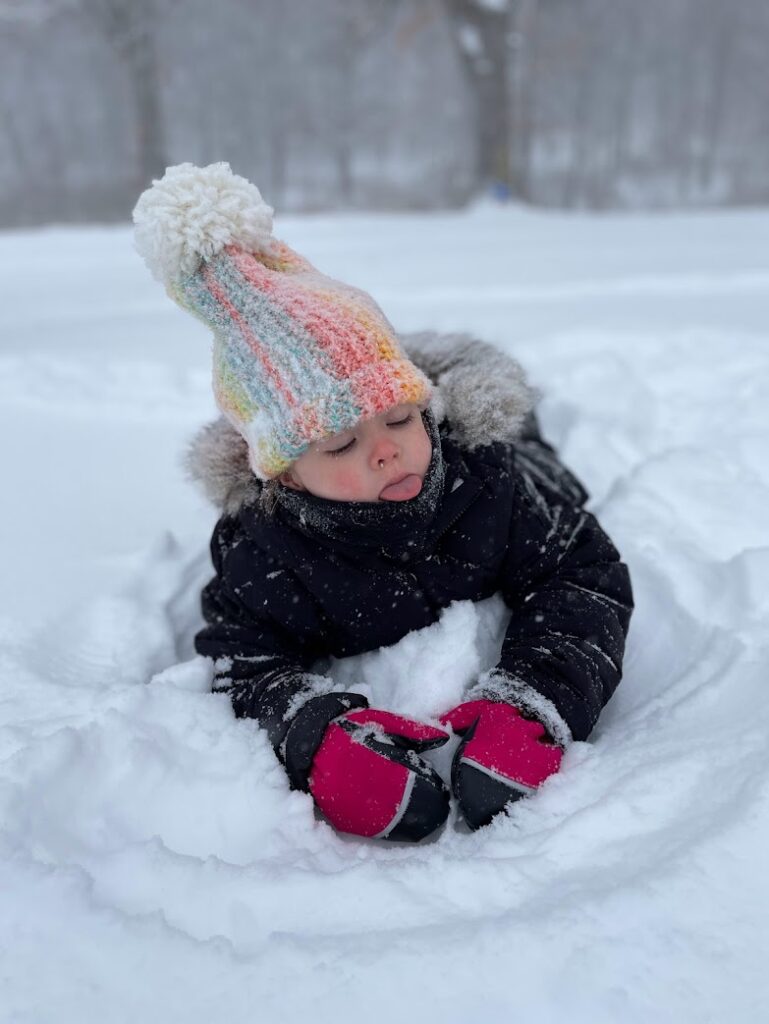 A girl laying in the snow with her tongue out trying to catch snowflakes