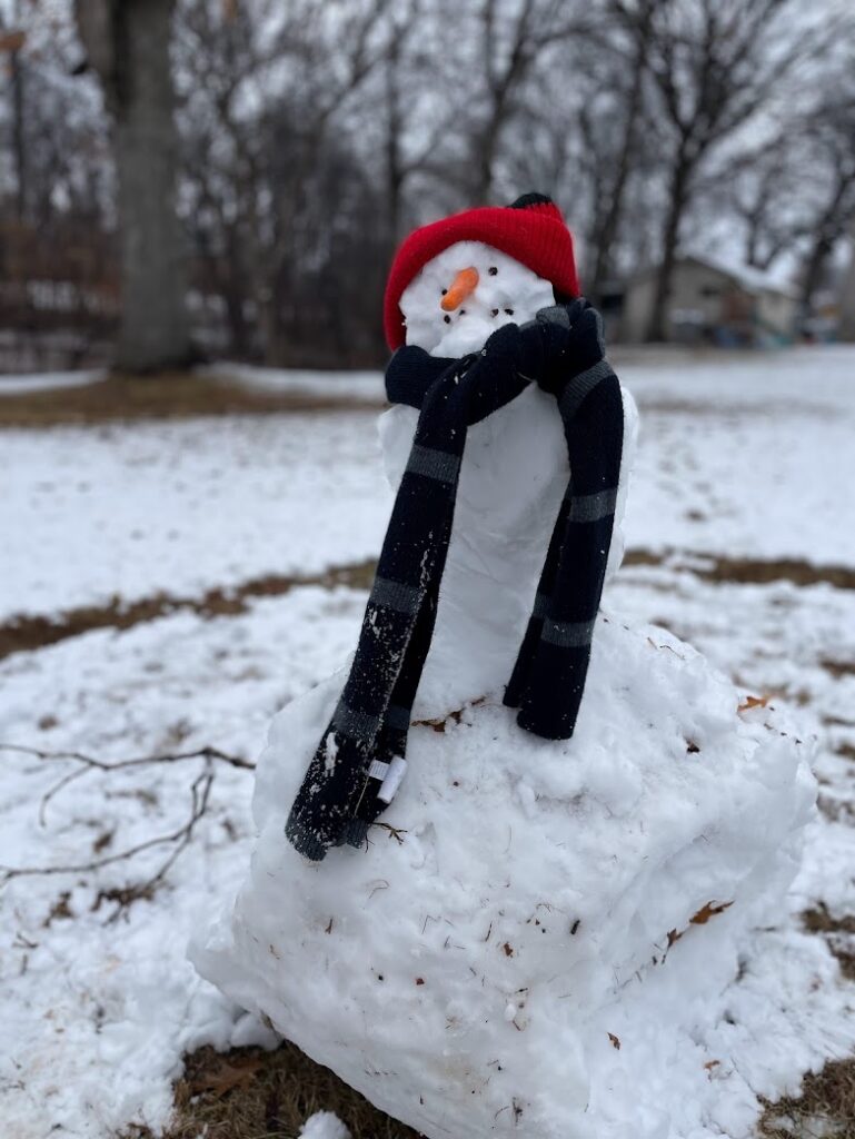 A cute snowman that is about three feet tall built by little kids