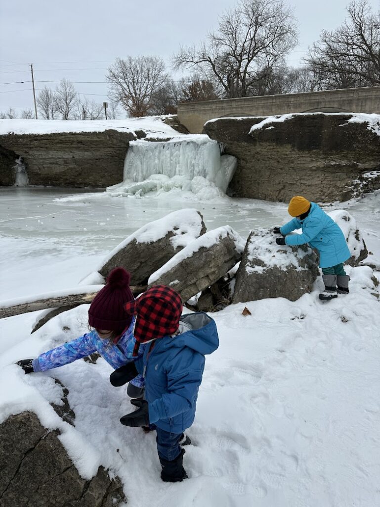 Three kids playing in the snow in front of a frozen waterfall