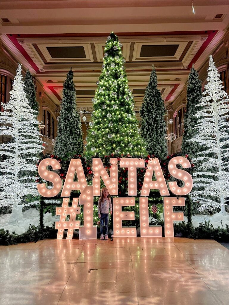 A girl standing with Santa's Number One Elf lit up sign at Union Station's Holiday Reflections 